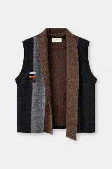 Chaleco abierto de lana, con diseño de bloques de color verticales en tonos marrón, gris y negro. Presenta un detalle de bordado artesanal con tres líneas horizontales en el frente y un ajuste holgado.