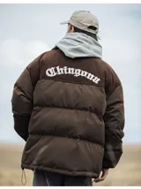 Campera puffer color nude (beige claro) con diseño acolchado. La parte superior de los hombros y el cuello son de pana acanalada. Presenta un bordado en la espalda con la palabra "Chingona" en tipografía gótica blanca. Posee tiras regulables en la cintura.
