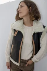 Chaleco estilo bomber de cuero negro con interior y detalles de piel sintética en color crema. Presenta cierre frontal con solapa de cuero en tono tostado y mangas de tejido de punto color crema.
