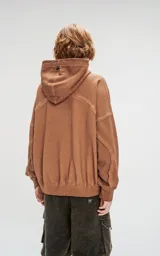 Hoodie oversize color beige con efecto batik, costuras expuestas y recortes estructurales. Presenta capucha amplia y bolsillo frontal tipo canguro.