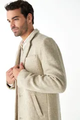 Abrigo masculino de lana color beige, con cuello con solapa, manga larga y forro interior. Tiene bolsillos laterales y cierre frontal con botones.