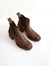 Bota tipo chelsea de cuero color chocolate con acabado texturizado, plataforma y taco cuadrado. Presenta paneles elásticos laterales en color negro.