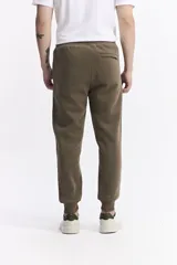 Pantalón de jogging color gris melange, confeccionado en tejido de algodón y poliéster. Presenta cintura elástica con cordón de ajuste, bolsillos laterales con cierre y puños elásticos en los tobillos.