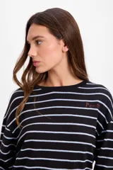 Remera de manga larga con diseño oversize, confeccionada en tejido de punto grueso a rayas horizontales en tonos marrón y blanco. Presenta cuello redondo y un pequeño bordado distintivo en el pecho.
