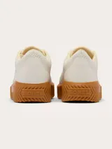 Zapatillas Sorel modelo Ona Ave Low, de diseño minimalista en color crema con suela de plataforma dentada en tono caramelo. Presenta cierre de cordones con ojales metálicos dorados y logo de la marca grabado en el lateral.