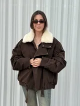 Campera de gamuza color marrón con cuello de corderito sintético en color crema. Presenta un diseño oversize con cierre frontal, solapas con broches metálicos y una tira ajustable en el ruedo.