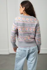 Cárdigan tejido de punto en color beige con diseño de flores y guardas caladas. Presenta escote en V, cierre frontal con botones y terminaciones acanaladas en puños y ruedo.