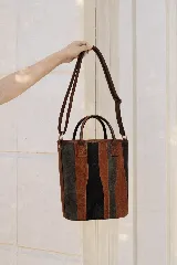 Matera de cuero con diseño de paneles verticales en combinación de colores azul, verde, marrón y bordó. Cuenta con dos asas cortas de cuero y estructura rígida.