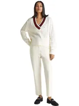 Sweater de punto color blanco hueso, con tejido trenzado (cableado) en el cuerpo y mangas. Presenta un cuello en V con ribete de rayas rojas y negras.