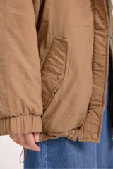 Campera acolchada reversible con capucha, diseño de matelassé, cierre frontal y puños elásticos. Presenta un lado en color verde oliva y otro en color beige.