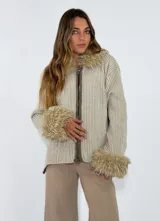 Saco de punto acanalado en color beige, con cierre frontal y detalles de piel sintética en el cuello y los puños.