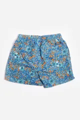 Short de baño celeste con estampado de hojas pequeñas en tonos verdes y blancos. Cuenta con cintura elástica con cordón ajustable, bolsillos laterales y un parche circular con logo en la parte inferior.