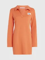 Vestido corto naranja de punto de algodón elástico con textura de canalé. Tiene cuello polo en V, mangas largas acampanadas e insignia con el monograma de Calvin Klein en el pecho.