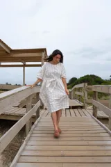 Túnica blanca con rayas verticales finas color dorado, corte holgado, mangas cortas amplias y lazo en la cintura.