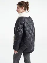 Chaqueta negra capitoneada con diseño de rombos, cuello de corderito blanco y paneles laterales de corderito a tono. Presenta cierre frontal con botones a presión.