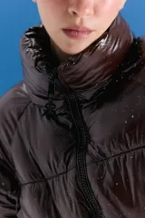 Campera puffer corta de acabado brillante en color marrón oscuro, con cuello alto, cierre frontal y diseño acolchado.