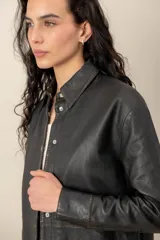 Camisa de cuero negro con efecto lavado, cuello camisero, cierre frontal con broches metálicos y mangas largas.