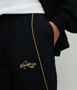 Pantalón deportivo de microfibra color negro, con corte holgado y diseño de piping contrastante en color amarillo. Cuenta con cintura elástica con cordón de ajuste, bolsillos laterales y logo bordado.