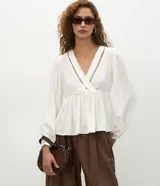 Blusa femenina tipo bata de viscosa color blanco, con escote en V cruzado y detalle calado. Presenta mangas largas con puños ajustados, corte amplio con recorte fruncido bajo el busto y diseño fluido.
