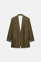 Blazer de lino color verde militar, con cuello solapa, hombreras y manga larga con puño revuelto con detalle a rayas. Cuenta con cierre frontal de un botón y bolsillos delanteros con solapa.