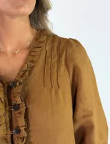 Vestido largo de lino color marrón tostado, con mangas 3/4 abullonadas, escote en V con volados y botones frontales. Cuenta con bolsillos laterales y detalle de volado en el dobladillo inferior.