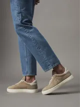 Zapatillas bajas de cuero color beige con logo CK bordado en el lateral y suela blanca con el nombre de la marca.