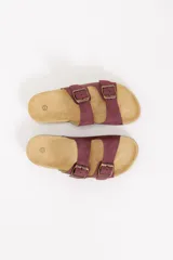 Sandalia plana estilo Birkenstock color bordó, con doble tira ajustable mediante hebillas metálicas en tono bronce y suela de corcho con base de goma.