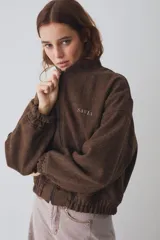 Campera bomber marrón de paño de lana, con cierre frontal, cuello de corderito sintético blanco desmontable, bolsillos laterales, puños y dobladillo elásticos, y logo bordado en el pecho.