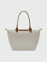 Mochila de diseño minimalista en color beige, con solapa y asa superior en cuero marrón texturizado. Cuenta con correas ajustables en color marrón y cierre principal.