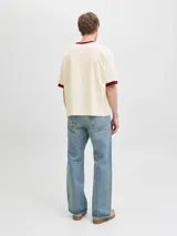 Remera de manga corta y cuello redondo, color blanco antiguo, con ribetes bordó en cuello y mangas. Presenta un estampado frontal con la palabra "ORIGINALS" y "studio" en azul marino, junto a pequeños textos y el número "1990".