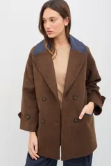 Tapado de paño de lana color marrón con silueta oversize y hombros caídos. Presenta doble abotonadura frontal, solapas amplias con detalle en contraste azul, y mangas con ajuste en los puños.