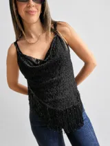 Blusa sin mangas de encaje negro con escote drapeado y bajo asimétrico adornado con flecos brillantes. Presenta breteles finos regulables y un diseño entallado.