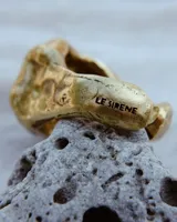 Anillo dorado con forma irregular y un agujero en el centro.