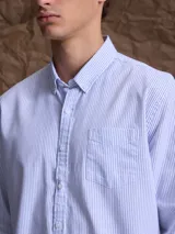 Camisa de corte clásico confeccionada en tejido Oxford de algodón, con diseño de rayas verticales finas en color azul y blanco, cuello abotonado y bolsillo frontal.