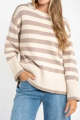 Sweater de punto con diseño a rayas horizontales en color negro y crema. Presenta cuello redondo, mangas largas con puños acanalados y un detalle de borde en tono bronce metalizado en el ruedo y los puños.