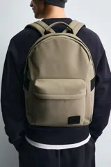 Mochila negra lisa con acabado engomado, compartimento principal con cierre de cremallera, bolsillo interior con cierre, bolsillo frontal con cierre, parte posterior acolchada con banda de sujeción para equipaje, asa de mano y dos asas de hombro ajustables y acolchadas.