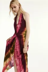 Vestido midi de cuello halter y escote en V, con diseño tie-dye en tonos fucsia, borgoña y verde. Presenta un nudo decorativo en el delantero, espalda descubierta y abertura frontal en el bajo.