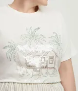 Remera de algodón blanca de manga corta y cuello redondo, con estampa frontal de palmeras y una casa de playa, acompañada por el texto "Summer feeling" y detalles de lentejuelas transparentes.