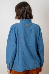 Camisa de pana color verde oliva, con cuello alto con volados, cierre frontal de botones y mangas largas con puños.