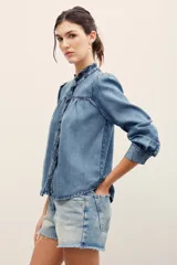 Camisa de denim de lyocell con cierre frontal de broches metálicos, cuello redondo con volados fruncidos y mangas largas con puños doblados.