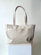 Cartera shopper clásica de cuero vacuno color beige, con doble asa de hombro, bolsillo frontal con broche magnético y cierre principal.