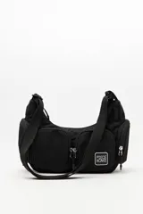 Cartera tipo shoulder color negro, de diseño utilitario y formato curvo. Confeccionada en material liviano y resistente, cuenta con correa regulable para llevar al hombro o cruzada. Incluye múltiples bolsillos con cierre en el frente y laterales, y un parche con el logo "Piece & Cake" en blanco.