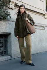 Chaqueta de algodón encerado con diseño de cuadros en tonos verde oliva, beige y líneas rojas. Presenta cuello solapa, cierre frontal con botones a presión metálicos, bolsillos de plastrón con solapa y un detalle de pañuelo desmontable sobre los hombros.