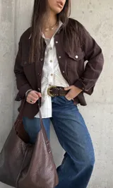 Sobrecamisa de gabardina color marrón chocolate, de corte holgado, con bolsillos con solapa en el pecho, mangas largas y cierre frontal de botones metálicos.
