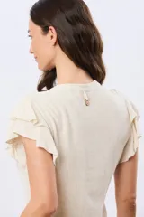 Camisa de lino y viscosa color beige, con cuello mao, escote en V y botones frontales de madera. Presenta mangas cortas con volados delicados.