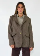 Blazer de corte clásico con textura de tejido de punto, color beige con detalles moteados. Presenta solapas tradicionales, cierre frontal de un botón, bolsillos laterales con solapa y bordes con acabado desflecado.