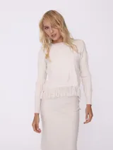 Sweater color beige de tejido de punto trenzado con cuello redondo y mangas largas. Presenta detalle de flecos en el ruedo.