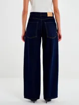 Jeans de denim color azul oscuro, tiro alto, con corte recto y pierna ancha (wide leg). Presentan costuras en hilo mostaza y cierre con botón metálico.