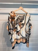 Blusa de satén con corte amplio y fluido, manga corta tipo kimono y cuello redondo. Presenta un estampado vibrante que combina motivos florales con cadenas y detalles geométricos en tonos beige, marrón, negro y naranja.