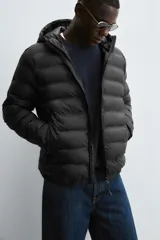 Campera puffer acolchada de corte regular fit en color negro, confeccionada en tejido técnico repelente al agua. Presenta cuello subido con capucha, cierre frontal de cremallera, mangas largas con puños elásticos y bolsillos laterales de vivo.